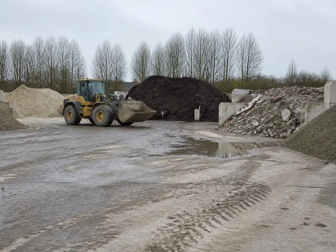 Shovel op een gronddepot met gescheiden hopen zand, grond en granulaat