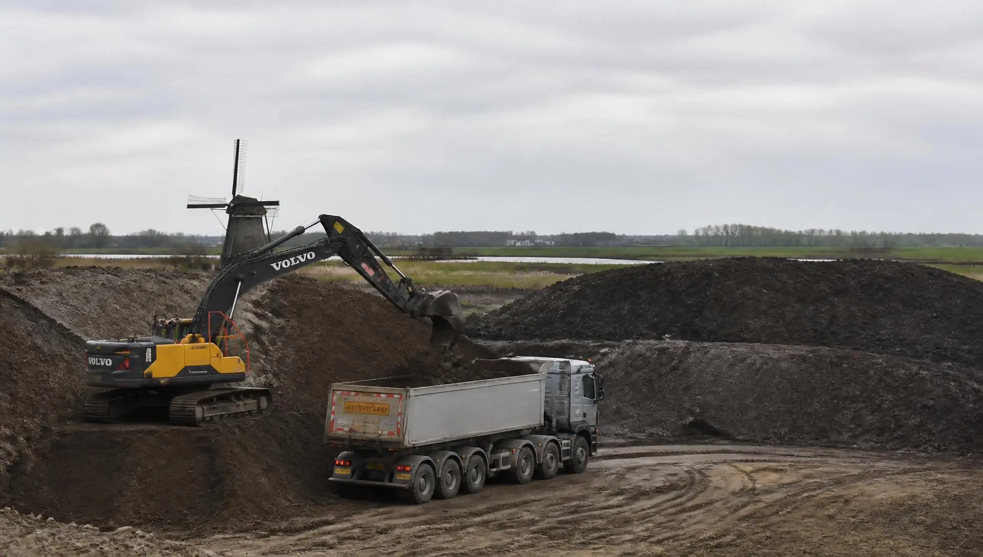 Graafmachine laadt grond in een kipper op een gronddepot in het Friese landschap